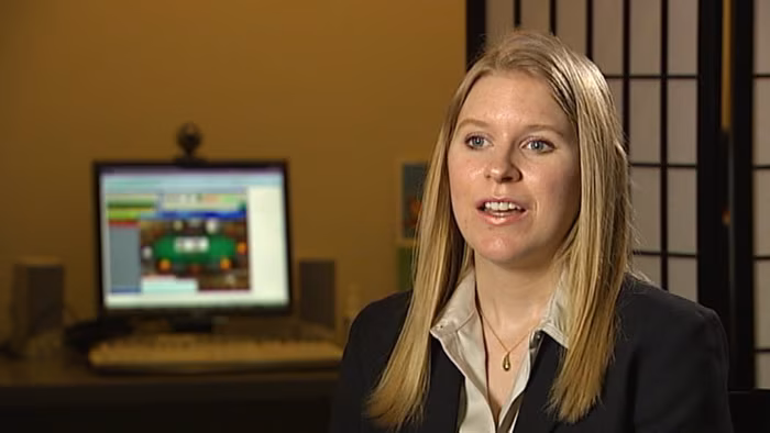 Photo d’une autrice blonde en veste sombre, assise dans un bureau devant un écran d’ordinateur